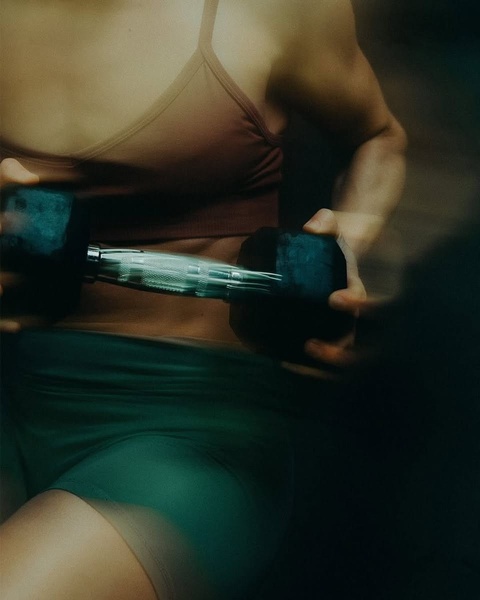 A close-up, motion-blurred shot of a person using a dumbbell, emphasizing intensity and physical exertion in a dimly lit, high-contrast environment.